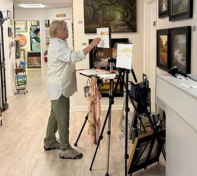 An artist painting at an easel inside the gallery